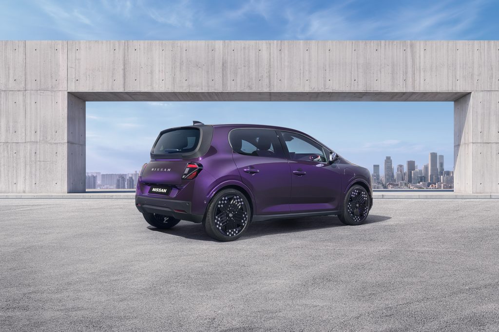Three-quarter rear view of a purple Nissan PIXO electric city car parked beneath a modern concrete structure, with a city skyline in the background.
